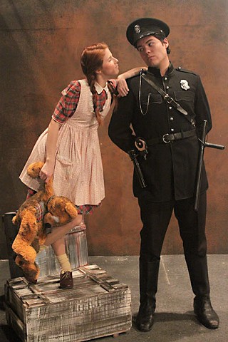 Little Sally (Sydney Roberts) consults Officer Lockstock (Gabriel Bernal) about exposition in <i>Urinetown</i>.